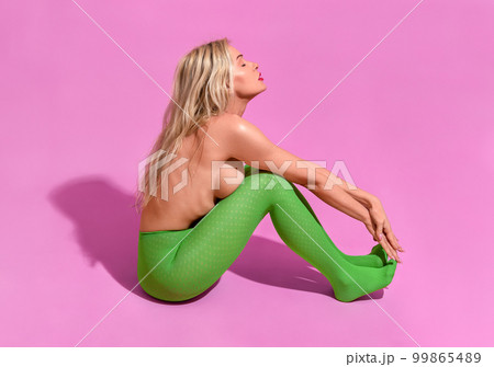 Fit woman with long blonde hair, in green tights and topless, minimalist on a purple background Fit woman with long blonde hair, in green tights and topless, minimalist on a purple background 99865489
