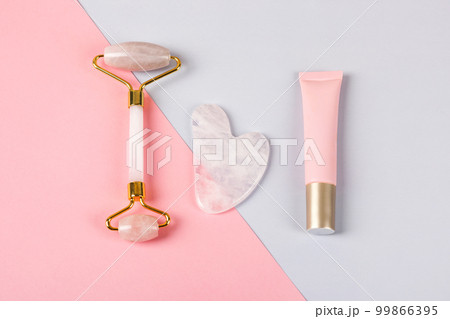 Pink jade roller and gua sha for face massage with cream or gel for the face. Facial massager tools. Anti age, lifting and toning care. Modern selfcare concept. Flat lay style. Pink jade roller and gua sha for face massage with cream or gel for the face. Facial massager tools. Anti age, lifting and toning care. Modern selfcare concept. Flat lay style. 99866395