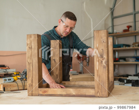 Male carpenter finishing work on wooden table in workshop. Male carpenter finishing work on wooden table in workshop. 99867984