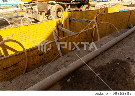 Excavator filling deep excavation supported by trench box with pipe bedding pea gravel during installation of drainage pipe. 99868385