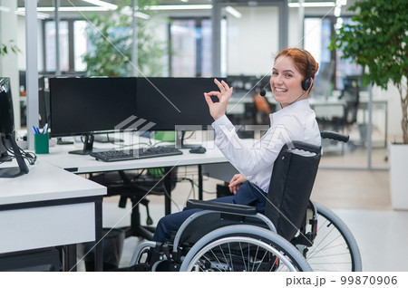 Caucasian woman in wheelchair showing ok sign while sitting in open space office. Caucasian woman in wheelchair showing ok sign while sitting in open space office. 99870906
