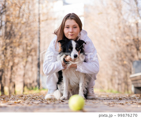 Caucasian woman hugging her dog on a walk in the autumn park. Border collie looks at the ball. Caucasian woman hugging her dog on a walk in the autumn park. Border collie looks at the ball. 99876270