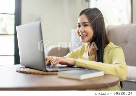 Young woman is sitting to smiling on the floor and using laptop to typing business report while working Young woman is sitting to smiling on the floor and using laptop to typing business report while working 99880324