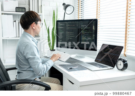 Male programmer is programming to develop program app and website of corporate while working to checking program code and debugging on multiple screen at modern software office 99880467