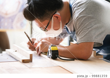 A carpenter measures the planks to assemble the parts and build a wooden table for the customer. 99881359