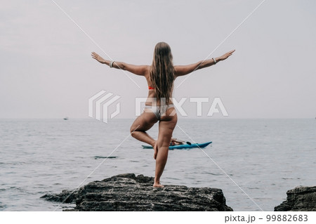 Woman sea yoga. Back view of free calm bliss satisfied woman with long hair standing on top rock with yoga position against of sky by the sea. Healthy lifestyle outdoors in nature, fitness concept. 99882683