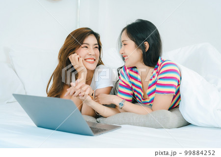 lgbtq, lgbt concept, homosexuality, portrait of two asian women posing happy together and loving each other while playing computer laptop on bed. 99884252