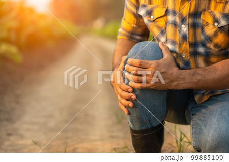 Injuries or Illnesses, that can happen to farmers while working. Man is using his hand to cover over knee because of hurt, pain or feeling ill. Injuries or Illnesses, that can happen to farmers while working. Man is using his hand to cover over knee because of hurt, pain or feeling ill. 99885100