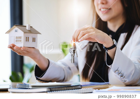 Accountant, businessman, real estate agent, Asian business woman handing house keys to customers along with house interest calculation documents for customers to sign 99890837