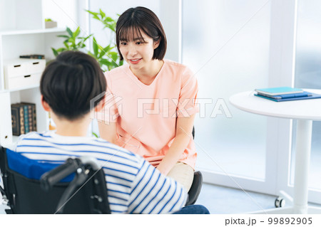 車椅子に乗った男の子を診察する女性医療従事者 99892905