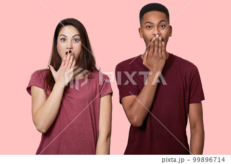 Waist up shot of surprised mixed race girlfriend and boyfriend being in stupor, cover mouth with palm, being shocked by terrific news, isolated over pink background. Diversity and reaction concept Waist up shot of surprised mixed race girlfriend and boyfriend being in stupor, cover mouth with palm, being shocked by terrific news, isolated over pink background. Diversity and reaction concept 99896714