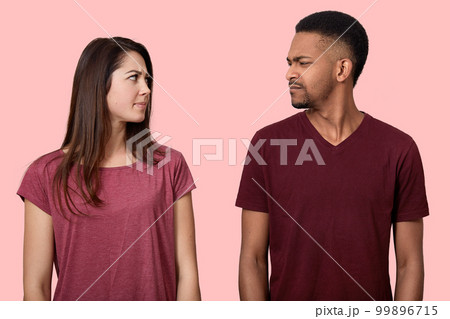Sullen displeased multiethnic lady and male looks with discontent at each other, frown faces, dont like something, wear t shirt, model over pink background. People, feeling and relationship concept Sullen displeased multiethnic lady and male looks with discontent at each other, frown faces, dont like something, wear t shirt, model over pink background. People, feeling and relationship concept 99896715