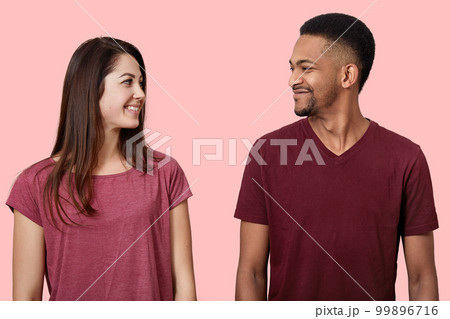 Close up image of happy young couple looking face to face at each other, stands smiling, dressed casual t shirts, enjoys spending time together, pose isolated over pink background in photo studio. Close up image of happy young couple looking face to face at each other, stands smiling, dressed casual t shirts, enjoys spending time together, pose isolated over pink background in photo studio. 99896716