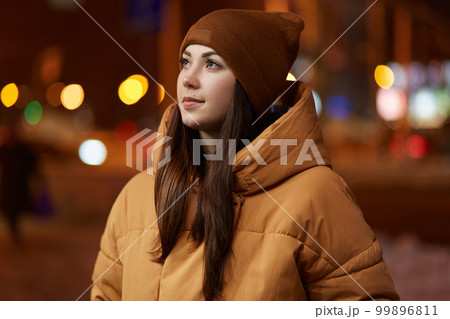 Outdoor shot of thoughtful young woman wears stylish hat and brown jacket, has pensive facial expression, enjoys calm atmosphere in evening city, poses over blurred background. Lifestyle concept Outdoor shot of thoughtful young woman wears stylish hat and brown jacket, has pensive facial expression, enjoys calm atmosphere in evening city, poses over blurred background. Lifestyle concept 99896811