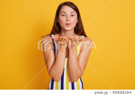 Horizontal shot of pleasant looking female with healthy skin, wearing swimsuit, making air kiss gesture, flirts with handsome guy at seaside, isolated over yellow studio background. People concept. 99898264