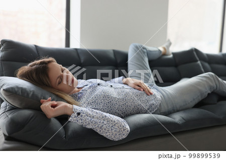 Woman feels tired and sleeps on sofa at home. 99899539