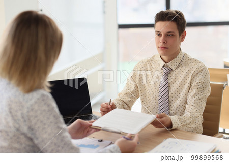 Managers pass documents to each other while sitting at their desks. 99899568