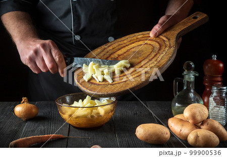 The chef prepares raw potatoes for lunch or dinner. Close-up of a cook hands while working in a restaurant kitchen The chef prepares raw potatoes for lunch or dinner. Close-up of a cook hands while working in a restaurant kitchen 99900536