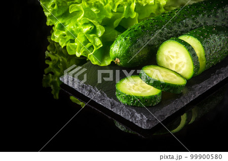 Set for cooking salad with herbs and sliced cucumbers on a black serving board. Vegetables containing vitamins 99900580