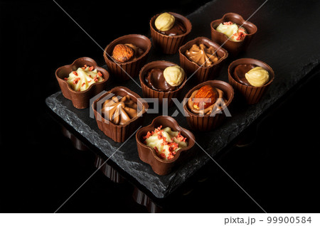 Candy with cream and nuts on a slate board. Assorted chocolate on black isolated background. Idea for dessert in restaurant Candy with cream and nuts on a slate board. Assorted chocolate on black isolated background. Idea for dessert in restaurant 99900584