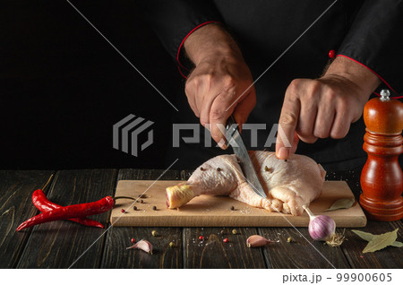 The cook cuts the chicken leg with a knife in the kitchen. The concept of a recipe for a delicious chicken meal with spices for a hotel or restaurant The cook cuts the chicken leg with a knife in the kitchen. The concept of a recipe for a delicious chicken meal with spices for a hotel or restaurant 99900605