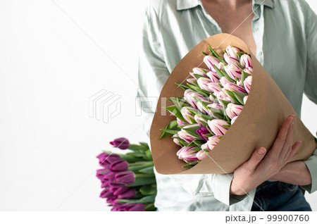 A large bouquet of tulips of different colors in the hands of a woman 99900760