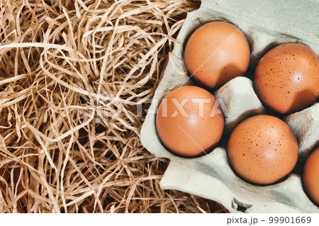 Close-up of brown chicken's eggs in a cardboard carton against straw background 99901669