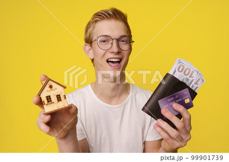 Financing Home Purchase Concept. A happy young man holds in his hands a wallet with money and a credit card to buy his home. High quality photo Financing Home Purchase Concept. A happy young man holds in his hands a wallet with money and a credit card to buy his home. High quality photo 99901739