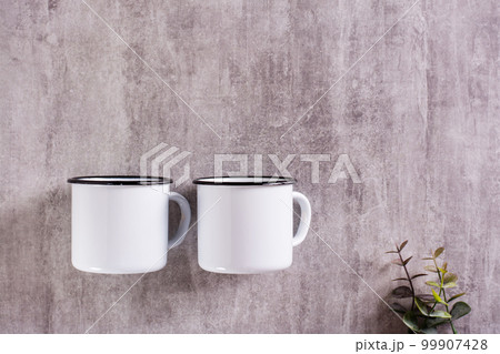 Two white empty metal mugs on a gray background with a place for an inscription. Top view 99907428