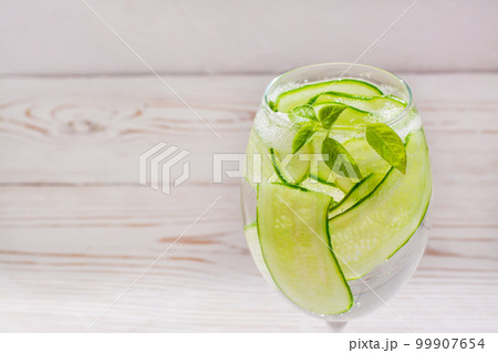 Refreshing water with slices of cucumber and basil leaves in a glass Refreshing water with slices of cucumber and basil leaves in a glass 99907654