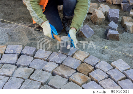 Worker were using industrial cobblestones to pave sidewalk with granite stones. 99910035