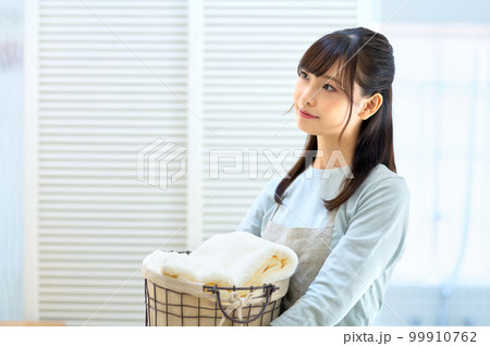 バスルームで洗濯物を運ぶエプロンを着た笑顔の若い主婦 99910762
