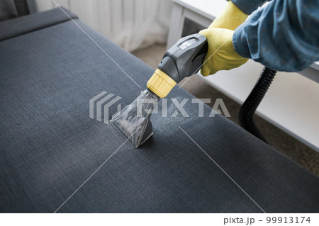 Man holding modern washing vacuum cleaner and cleaning dirty sofa with professionally detergent. Professional springclean at home concept Man holding modern washing vacuum cleaner and cleaning dirty sofa with professionally detergent. Professional springclean at home concept 99913174