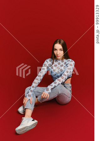 Young woman in tank top and jeans posing on the floor of red studio Young woman in tank top and jeans posing on the floor of red studio 99913329