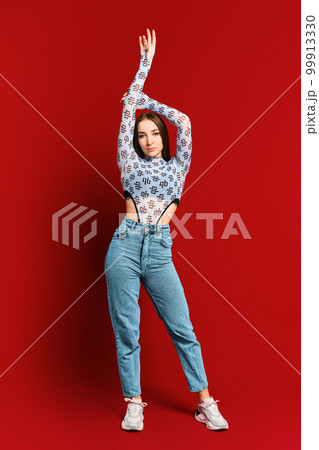 Young woman posing on red wall background with lifted arm Young woman posing on red wall background with lifted arm 99913330