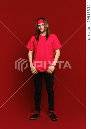 Indoor portrait of positive good-looking hipster guy wearing red band on head, standing against red wall Indoor portrait of positive good-looking hipster guy wearing red band on head, standing against red wall 99913334