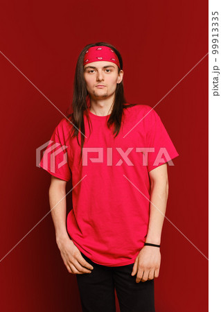 Portrait of positive guy wearing red band on head and shirt, standing against red wall Portrait of positive guy wearing red band on head and shirt, standing against red wall 99913335