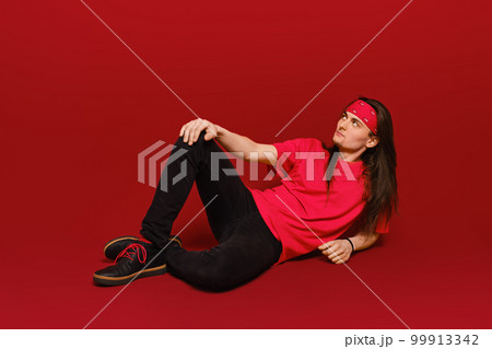 Man with long hair sitting on floor in red studio 99913342