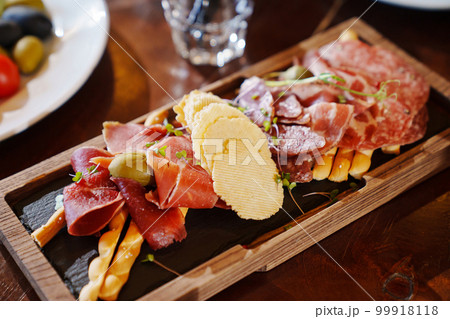 a wooden tray with snacks made of dried meat, sausage, cheese and potato chips. a wooden tray with snacks made of dried meat, sausage, cheese and potato chips. 99918118