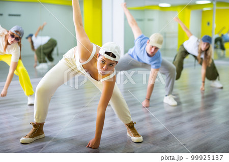 Dancer boys and girls showing different tricks and movements while dancing in studio, flexible and sportive female on floor 99925137