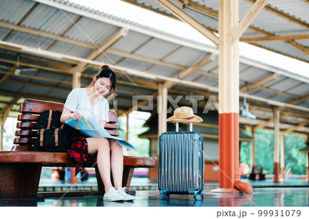 summer, relax, vacation, travel, portrait of a cute Asian girl looking at a map to plan a trip while waiting at the train station 99931079