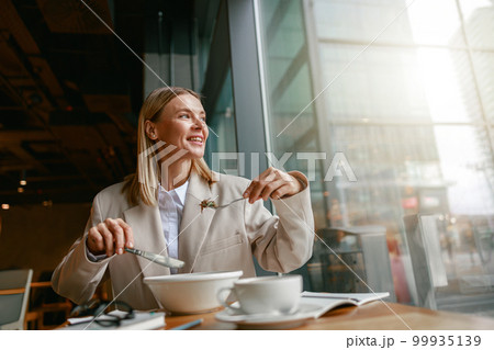 Cheerful businesswoman is having a business lunch during working day in cafe. Blurred background Cheerful businesswoman is having a business lunch during working day in cafe. Blurred background 99935139
