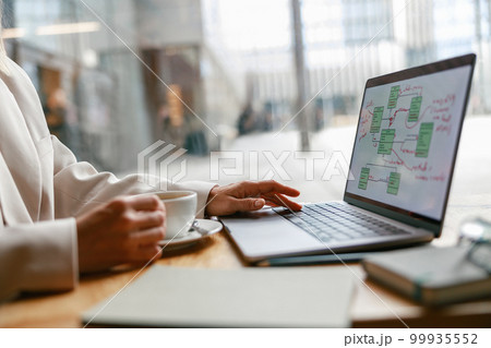 Close up of woman freelancer working on laptop and drinking coffee while sitting in cafe near window Close up of woman freelancer working on laptop and drinking coffee while sitting in cafe near window 99935552