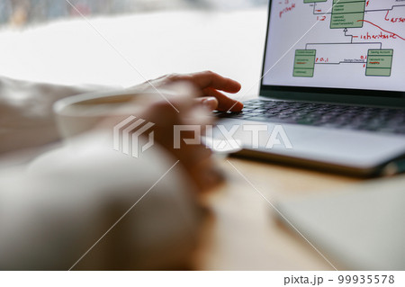 Close up of woman freelancer working on laptop and drinking coffee while sitting in cafe near window 99935578