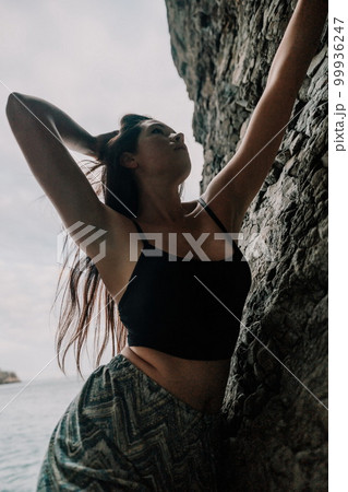 Sports Woman Climbing The Rock. Young woman With slim fit body climbing in volcanic basalt cave with beautiful sea view. The athlete girl trains in nature. Woman overcomes difficult climbing route. Sports Woman Climbing The Rock. Young woman With slim fit body climbing in volcanic basalt cave with beautiful sea view. The athlete girl trains in nature. Woman overcomes difficult climbing route. 99936247