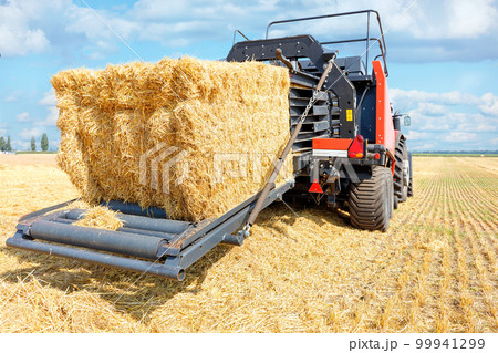 A modern agricultural machine collects straw into large bales after the end of the wheat harvest. 99941299