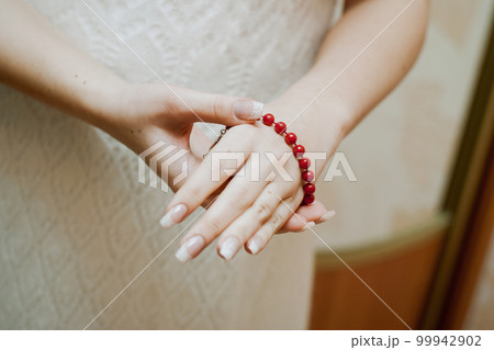 The bride puts on a red bracelet on her hand. close-up of hands The bride puts on a red bracelet on her hand. close-up of hands 99942902