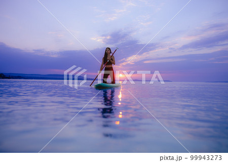 Young beautiful girl surfer paddling on surfboard on the lake at sunrise 99943273