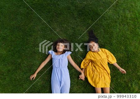 Happy friends lying in the grass, holding each other hands and having fun. Top view. Happy friends lying in the grass, holding each other hands and having fun. Top view. 99943310