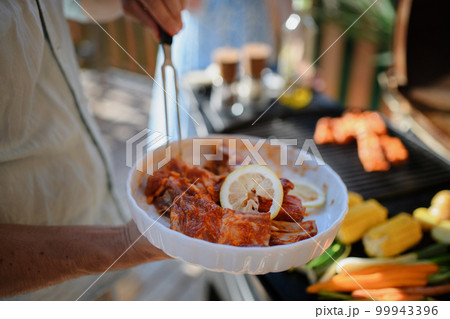 Unrecognizable man preparing meat and vegetables for grilling during family summer garden party, close-up 99943396
